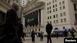 Pedestrians walk past a banner with the Spotify logo on it as the company lists its stock on the New York Stock Exchange with a direct listing in New York, April 3, 2018.
