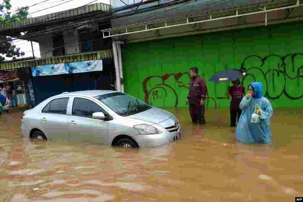 جکارتہ میں کچھ لوگ زیرِ آب آجانے والی کار کے قریب سے گزر رہے ہیں۔ رات بھر کی بارش نے سیلابی صورتِ حال پیدا کردی جس سے شہریوں کو سخت دشواری کا سامنا کرنا پڑا۔&nbsp; &nbsp;