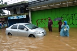 Warga berjalan melintas di depan mobil yang terjebak banjir di Jakarta, 1 Januari 2020. (Foto: AFP)