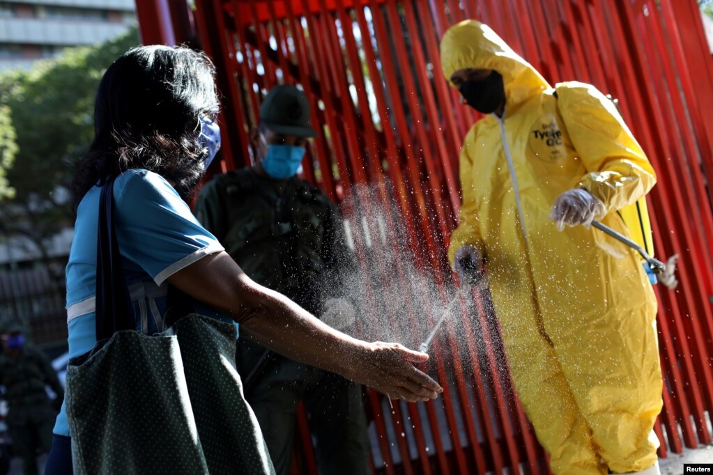 Un trabajador con traje protector desinfecta las manos de un cliente en la entrada de un mercado público en respuesta a la propagación de la enfermedad por coronavirus (COVID-19) en Caracas, Venezuela.