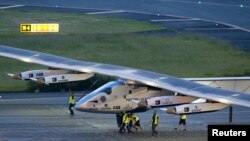 Crew members push the solar-powered plane Solar Impulse 2 to its parking position at Nagoya airport after changing weather conditions thwarted a planned take-off, June 24, 2015.