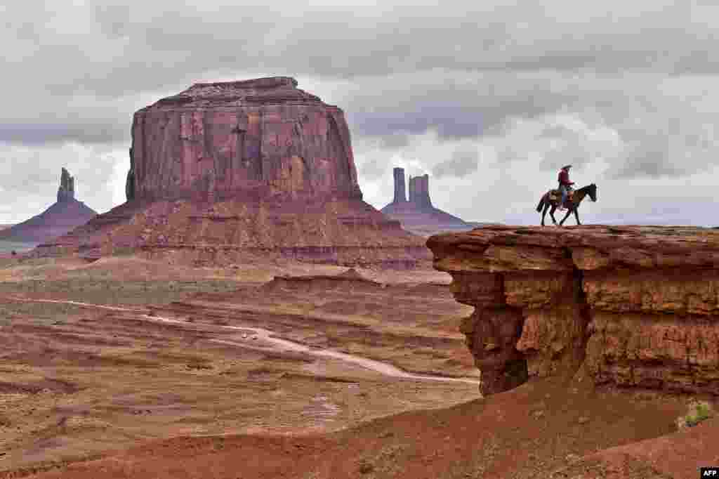 Seorang pria Navajo di atas kuda berpose di depan Merrick Butte di Monument Valley Navajo Tribal Park, Utah, USA.