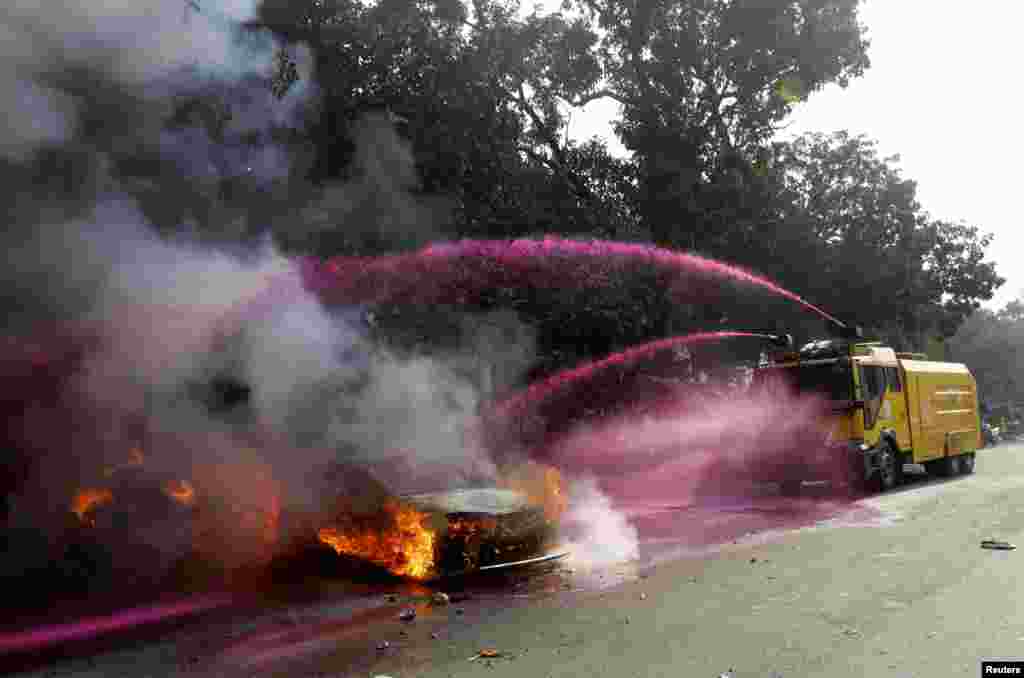 A police vehicle uses colored water to put out flames after vehicles were torched and vandalized by Jamaat-e-Islami party activists during clashes with police in Dhaka, Dec. 13, 2013.