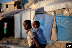 FILE - A boy carries his little brother to school, at a camp for people displaced by the 2010 earthquake, at what was once a golf club, in Port-au-Prince, Haiti.