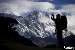 FILE - A tourist is silhouetted as he takes pictures of Mount Nuptse (C) as Mount Everest (L) is covered with clouds in Solukhumbu district, also known as the Everest region, Nov. 30, 2015.