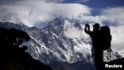 FILE - A tourist is silhouetted as he takes pictures of Mount Nuptse, center, as Mount Everest, left, is covered with clouds in Solukhumbu district, also known as the Everest region, Nov. 30, 2015.
