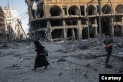 A woman walks past bombed-out buildings in Gaza, in this image captured by Fatima Shbair during the 11-day war in May 2021. Shbair risked her life to photograph scenes from the war. (Photo by Fatima Shbair/Courtesy of Getty Images)