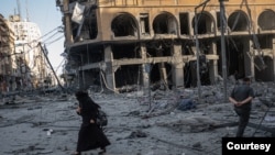 بمباری سے غزہ کی تباہ شدہ عمارت کے سامنے گزرنے والی خاتون کی یہ تصویر فلسطینی فوٹو جرنلسٹ فاطمہ شبیر نے مئی میں فلسطین اور اسرائیل کے درمیان ہونے والے تنازعے کے دوران لی تھی۔