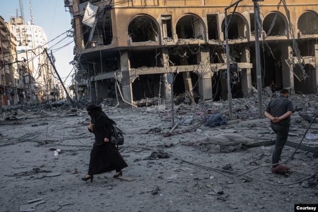 A woman walks past bombed-out buildings in Gaza, in this image captured by Fatima Shbair during the 11-day war in May 2021. Shbair risked her life to photograph scenes from the war. (Photo by Fatima Shbair/Courtesy of Getty Images)
