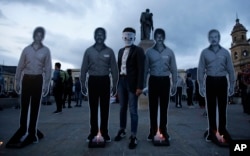 A demonstrator poses for a photo next to cardboard cutouts representing slain activists during a candle light vigil for those who have been killed since the signing of the peace accords in Bogota, Colombia, July 6, 2018.