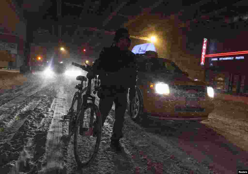 Phụ nữ dắt xe đạp đi qua đường phố trơn trượt vì bão tuyết ở New York, ngày 3/1/2014. 