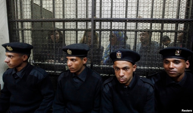 FILE - Some of the 14 Egyptian activists who were accused of working for unlicensed nongovernmental organizations (NGOs) and receiving illegal foreign funds stand in a cage during the opening of their trial in Cairo, Feb. 26, 2012.
