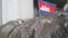 FILE: A Cambodian National flag flutters above barbed wire set up by police near the Council of Ministers building while garment workers gather for a rally in Phnom Penh, Cambodia, Monday, Dec. 30, 2013. 