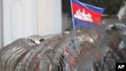 FILE: A Cambodian National flag flutters above barbed wire set up by police near the Council of Ministers building while garment workers gather for a rally in Phnom Penh, Cambodia, Monday, Dec. 30, 2013. 