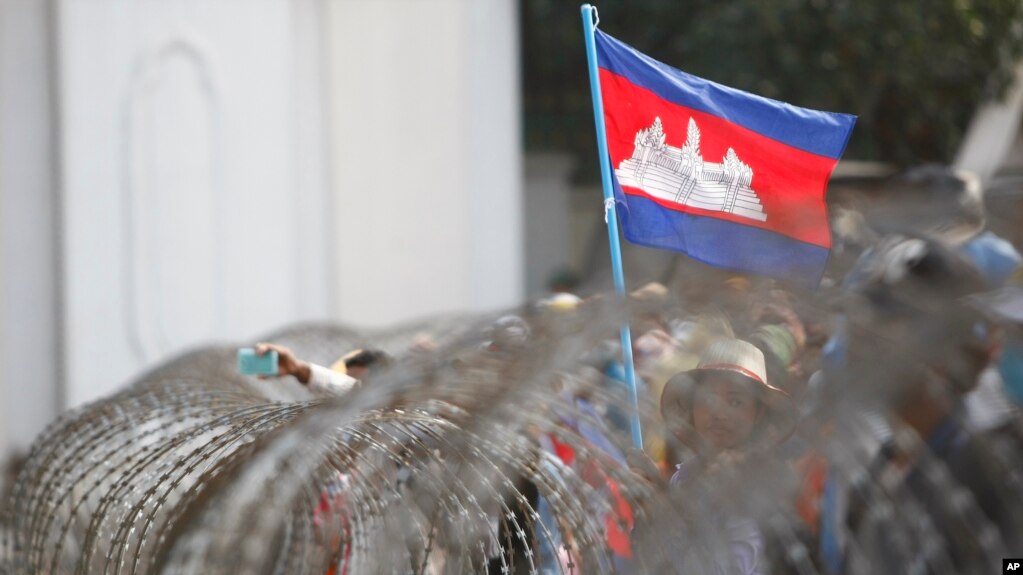 រូបឯកសារ៖ ទង់ជាតិខ្មេរត្រូវបានដោតលើរបងលួសដែលប៉ូលិសបានដាក់បិទច្រកចូលអគាររបស់ទីស្តីការគណៈរដ្ឋមន្ត្រី ក្នុងអំឡុងពេលបាតុកម្មមួយដែលធ្វើឡើងដោយកម្មកររោងចក្រទាមទារការដំឡើងប្រាក់ឈ្នួល នៅរាជធានីភ្នំពេញ កាលពីថ្ងៃទី ៣០ ខែធ្នូ ឆ្នាំ ២០១៣។