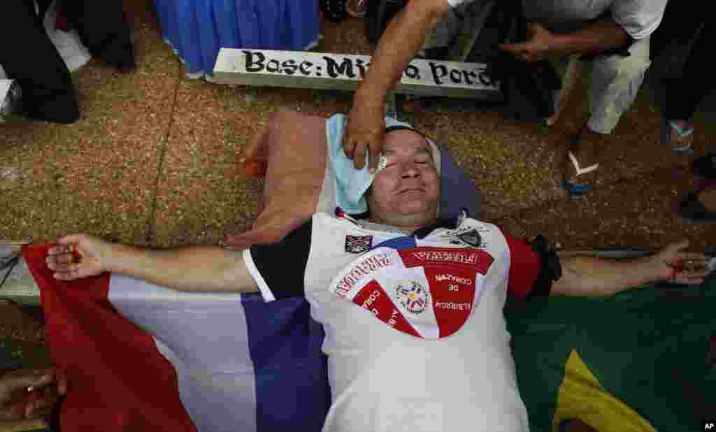 A fellow protester wipes the eye of Gerardo Orue as he lies crucified outside Brazil&#39;s embassy in Asuncion, Paraguay. Former workers of a company contracted to build the Itaipu Dam on the Brazil-Paraguay border are demanding compensation for those let go.