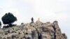 FILE - A Hezbollah fighter stands on a hill next to the group's yellow flag at Assal al-Ward, Syria, May 9, 2015. Experts say Iran's sending Afghan refugees to fight on the Syrian front, alongside Hezbollah and Iranian forces, has long-term implications for Afghanistan and the region at large.