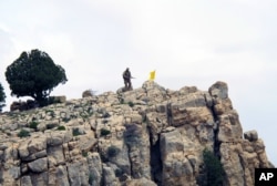 FILE - A Hezbollah fighter stands on a hill next to the group's yellow flag in the fields of Assal al-Ward, Syria, May 9, 2015.