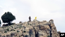 FILE - A Hezbollah fighter stands on a hill next to the group's yellow flag in the fields of Assal al-Ward, Syria.