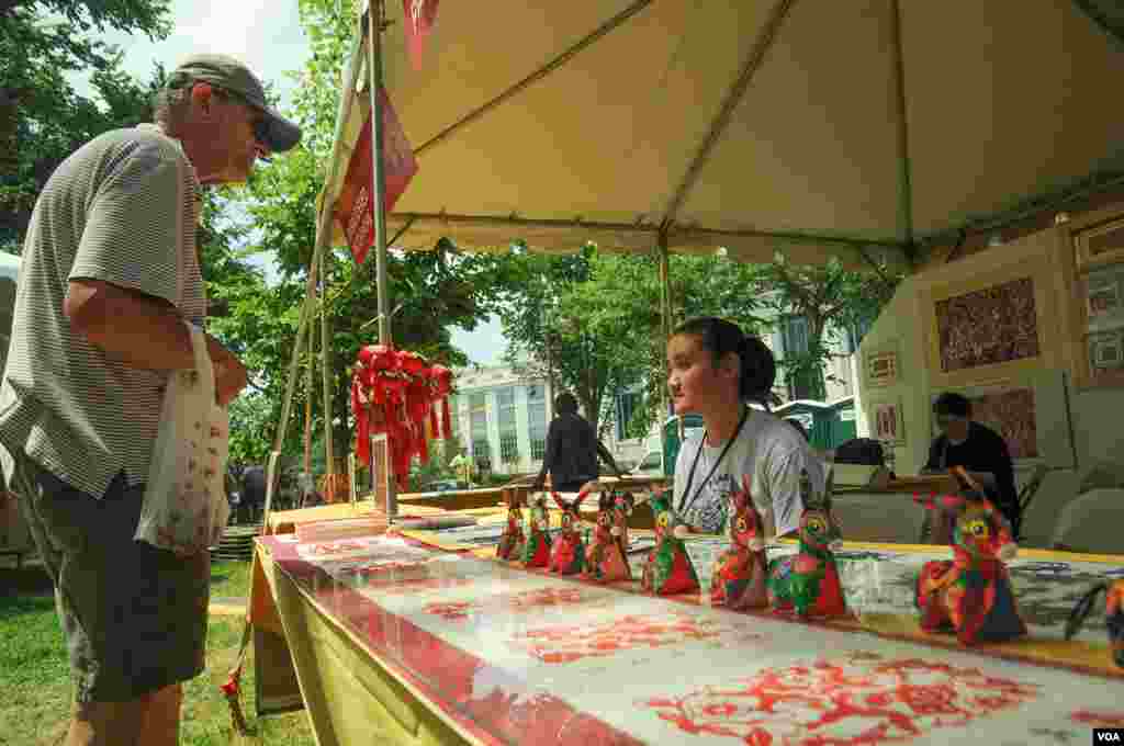 A young woman and a visitor talk in the market place of the Smithsonian Folklife Festival in Washington, June 25, 2014. (Regina Catipon/VOA)