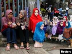 Dua perempuan duduk dekat boneka peraga yang mengenakan hijab-hijab untuk dijual di Pasar Tanah Abang menjelang bulan Ramadan, Jakarta, 27 Juni 2014.