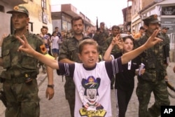 A boy sings in the street as Kosovo Liberation Army soldiers march into Prizren on June 15, 1999, to celebrate the departure of Serb forces and the arrival of German NATO troops.