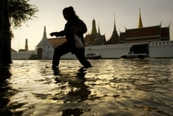 Seorang wanita berjalan melalui air banjir di depan Grand Palace dekat sungai Chao Praya di Bangkok. (Foto: AFP)