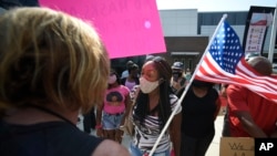 FILE - Pro-mask wearing demonstrator Djenaba Pershay, center, speaks with a non-mask demonstrator, left, at the Cobb County School Board Headquarters during a pro mask wearing protest, in Marietta, Ga., Aug. 12, 2021.