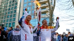 IOC President Thomas Bach, right, hands over the Olympic torch to United Nations Secretary-General Ban Ki-moon as the torch relay arrives in Sochi, ahead of the 2014 Winter Olympics, Feb. 6, 2014, in Russia.