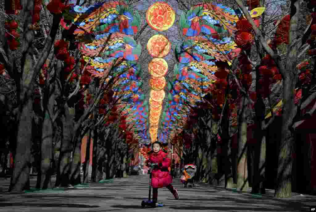 A girl rides on a scooter under decorations for a temple fair ahead of Chinese Lunar New Year at Ditan Park in Beijing, China.