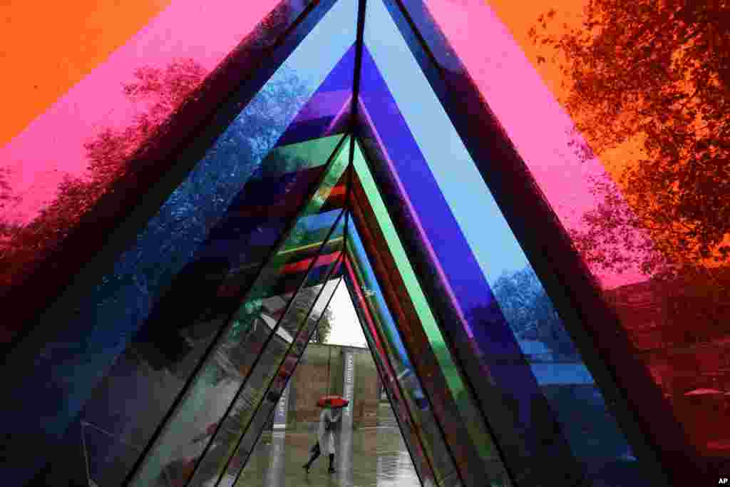 A woman shelters with an umbrella as she walks past an artwork by artist Liz West, part of the Kensington and Chelsea art week, outside the Saatchi Gallery in London.