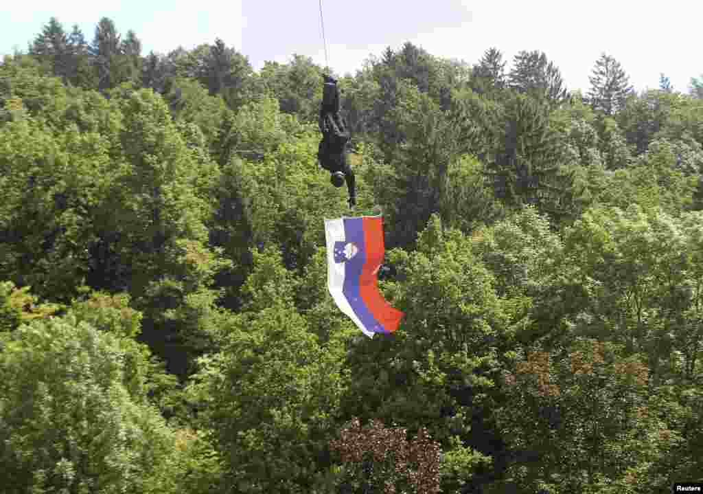 A member of the Special Police Unit (SEP) holds a Slovenian flag as he descends from a helicopter during an event to celebrate the 40th anniversary of the establishment of their unit, in Tacen.