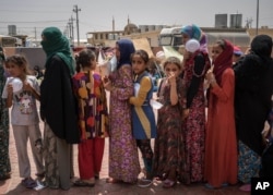 FILE - Women and children stand in line for food at Dibaga camp for internally displaced civilians in Iraq, Aug. 7, 2016. Some say the announcement about the return of refugees is politically driven to make the impending battle for Mosul more "palatable."