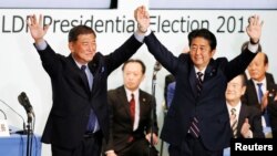 Perdana Menteri Jepang, Shinzo Abe (kanan) yang juga pemimpin Partai Yang Berkuasa, Partai Demokratik Liberal, mengangkat tangannya bersama mantan Menhan Shigeru Ishiba pasca diumumkannya kemenangan Abe sebagai pemimpin partai melalui pemungutan suara di markas besarnya di Tokyo, 20 September 2018.