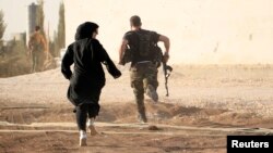 A woman reporter runs with a rebel fighter to avoid snipers at the frontline against the Islamic State fighters in Aleppo's northern countryside, Syria, Oct. 10, 2014.