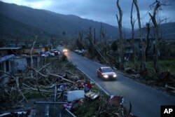 FILE - In this Sept. 26, 2017, file photo, neighbors sit on a couch outside their destroyed homes as sun sets in the aftermath of Hurricane Maria, in Yabucoa, Puerto Rico.