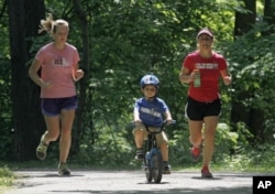 FILE - Andrea Lemastra, right, and Kim Walsh, left, jog on a wooded park trail while Lemastra's son, Luca rides his bike, in Lakewood, Ohio on May 24, 2012. (AP Photo/Mark Duncan)