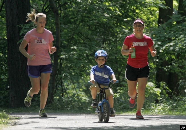 FILE - Andrea Lemastra, right, and Kim Walsh, left, jog on a wooded park trail while Lemastra's son, Luca rides his bike, in Lakewood, Ohio on May 24, 2012. (AP Photo/Mark Duncan)