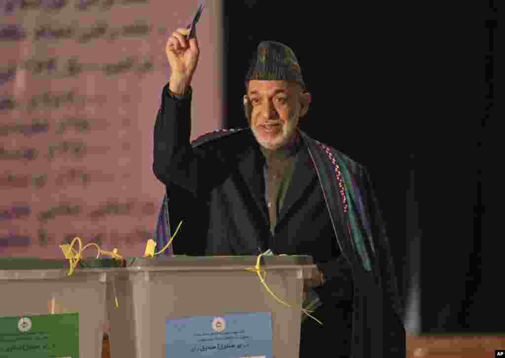 Afghan President Hamid Karzai shows his ballot paper to the media before he casts his vote at Amani high school, near presidential palace in Kabul, April 5, 2014.