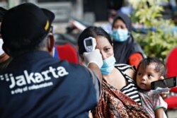 Seorang perempuan menggendong anaknya saat ia menjalani pemeriksaan kesehatan sebelum menerima vaksin COVID-19 dalam program vaksinasi bagi para pemulung di Jakarta, pada 10 Desember 2021. (Foto: Reuters/Ajeng Dinar Ulfiana)