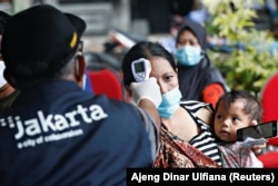 Seorang perempuan menggendong anaknya saat menjalani pemeriksaan kesehatan sebelum menerima vaksin COVID-19 dalam program vaksinasi bagi para pemulung di Jakarta, 10 Desember 2021. (Reuters/Ajeng Dinar Ulfiana)