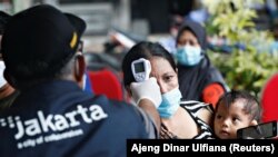 Seorang perempuan menggendong anaknya saat ia menjalani pemeriksaan kesehatan sebelum menerima vaksinasi COVID-19 di Jakarta. (Foto dok. Reuters/Ajeng Dinar Ulfiana)
