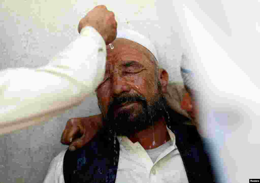 아프가니스탄 수도 카불에서 자살폭탄 공격으로 아들을 잃은 주민이 실신하자, 이웃이 물을 뿌리고 있다.