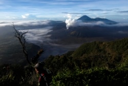 Seorang pengunjung berjalan saat gunung berapi Gunung Bromo Indonesia memuntahkan asap di sebelah gunung berapi Gunung Semeru (di latar belakang) seperti yang terlihat dari Gunung Penanjakan di luar Pasuruan, Jawa Timur, 14 September 2010. (Foto: REUTERS/