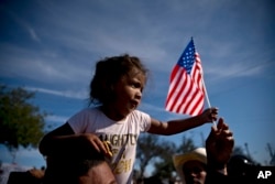A migrant girl with a U.S. flag sits on the shoulders of a man marching with other migrants to the Chaparral border crossing in Tijuana, Nov. 25, 2018, as they try to reach the U.S.