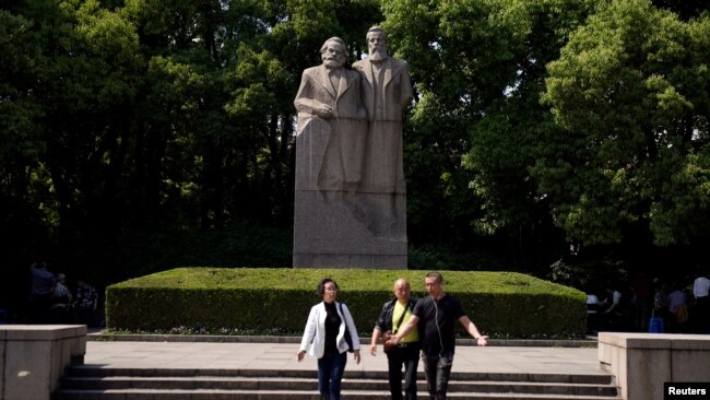 上海的一个公园里有共产主义理论家卡尔·马克思和弗里德里希·恩格斯的雕像。前面有三个人走过（2018年5月3日）。中共推崇马克思主义，限制外国学者在华研究。