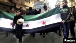 Un muchacho camina con pan en la mano en frente de una bandera de la oposición siria en Alepo.