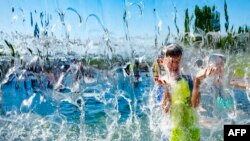 Seorang anak laki-laki bermain di air mancur di taman di Washington DC, untuk mendingin tubuh di tengah cuaca panas, 28 Juni 2021. 