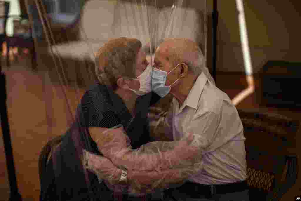 Agustina Cañamero, 81, and Pascual Pérez, 84, hug and kiss through a plastic film screen to avoid contracting the new coronavirus at a nursing home in Barcelona, Spain.