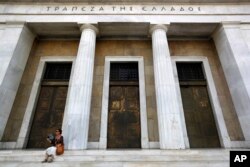 A woman uses her fan to cool down outside the Bank of Greece headquarters in Athens, July 24, 2017. Greece's bond sale on July 25, 2017, was the country's first attempt to return to international borrowing markets since a single bond issue in 2014.